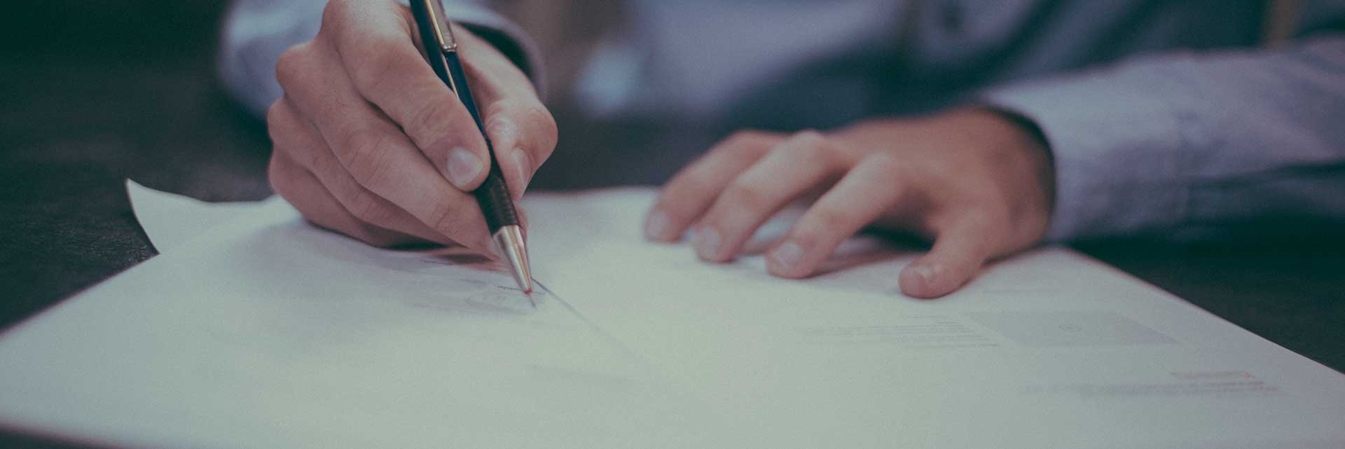 man using pen to write on papers