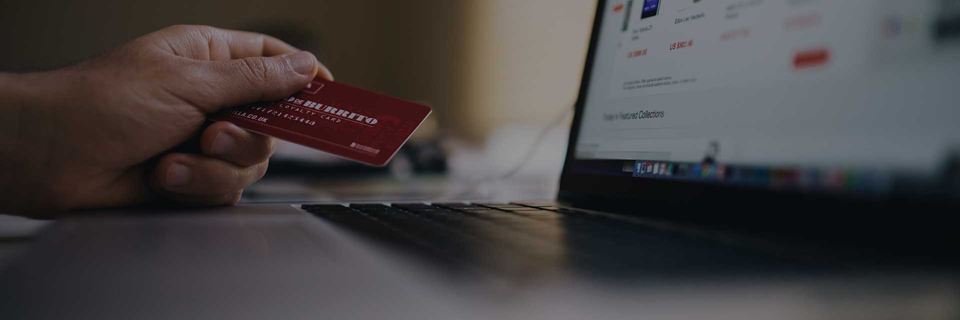 hand holding credit card next to laptop screen